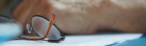 A pair of reading glasses resting on a legal document, with a blurred hand in the background, symbolizing the review of Articles of Association in Thailand.