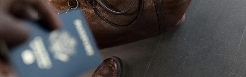 A person holding a passport near a leather travel bag, symbolizing international travel and visa processes, including the application for a long term resident visa.