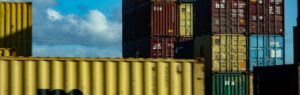 A stack of colorful shipping containers at a port, symbolizing international trade and business regulations, with a blurred yellow container in the foreground. The image represents the impact of the Foreign Business Act in Thailand on foreign trade and investment.