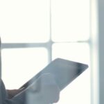 A professional holding a tablet in a bright, modern office with large windows, symbolizing efficiency and legal expertise in thai limited company