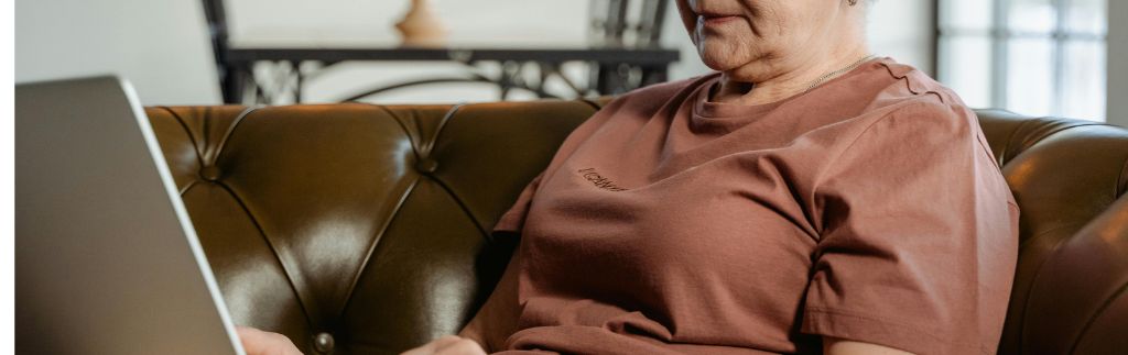 Elderly woman sitting on a leather couch using a laptop, focused on the screen in a well-lit living space looking for a Thailand Retirement Visa