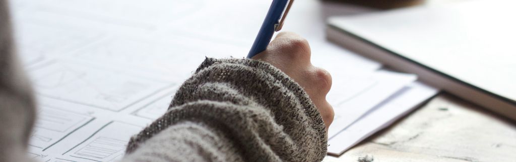 A person in a sweater writing on a document with a pen, symbolizing education, visa applications, or academic paperwork.