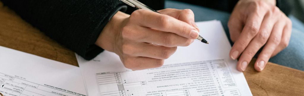 A person filling out a corporate income tax in Thailand form with a pen, focusing on financial documents on a wooden desk.