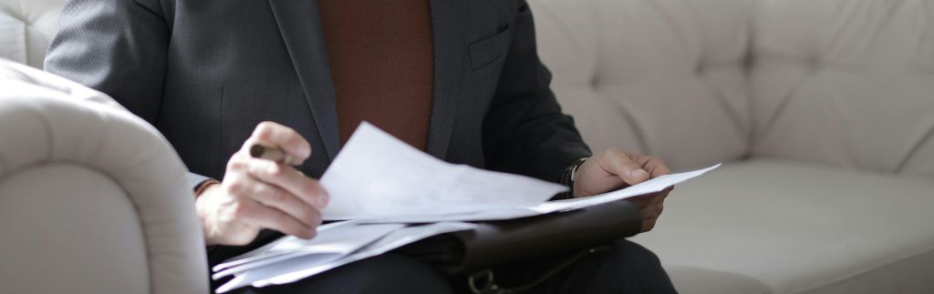 Un avocat en costume assis sur un canapé en cuir, tenant et examinant des documents juridiques, illustrant le concept du droit des contrats en Thaïlande.