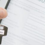 Hand holding a home key in front of a property insurance policy document in Thailand