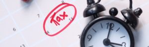 Календарь с выделенной красной ручкой датой "14" и пометкой "Tax", а также черный будильник, подчеркивающий срочность уплаты налоги в Таиланде.
