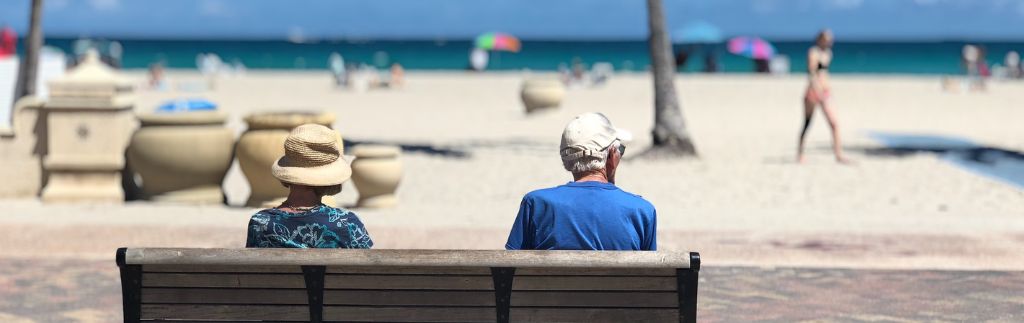 Retirement in Thailand: elderly couple sitting peacefully on a beach bench facing the sea