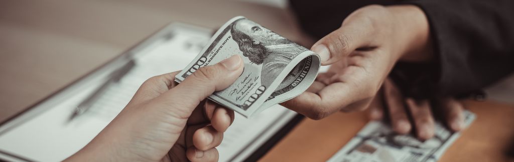 Una persona consegna una banconota a un’altra, simbolo del concetto di retribuzione e del salario minimo in Thailandia.
