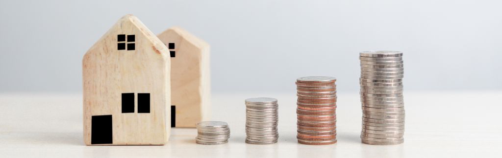 Miniature di case accanto a pile di monete crescenti, simbolo della crescita economica e degli investimenti immobiliari in Thailandia.