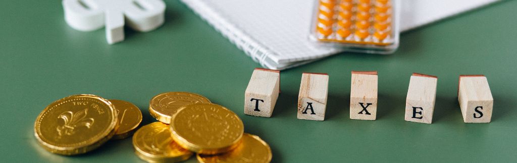 Monete dorate e blocchi di legno con la parola “TAXES” su sfondo verde, simbolo delle tasse in Thailandia.
