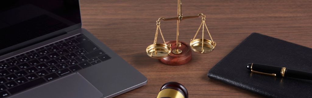 Bilancia della giustizia, computer portatile e penna su una scrivania, simbolo del diritto del lavoro e delle normative sui lavoratori stranieri in Thailandia.