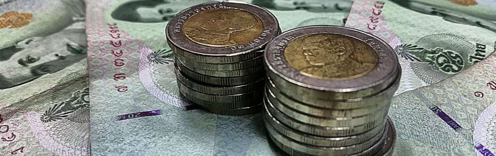 Münzen und thailändische Baht-Scheine als Symbol für den Mindestlohn in Thailand und die wirtschaftlichen Unterschiede im Land