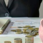 Personne en costume ajoutant une pièce dans une tirelire tout en gérant des documents financiers, illustrant les démarches pour ouvrir un compte bancaire en Thaïlande.