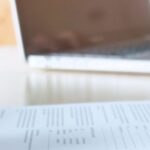 Une personne remplit le formulaire TM7 à la main devant un ordinateur portable, dans le cadre d’une demande d’extension de visa en Thaïlande.