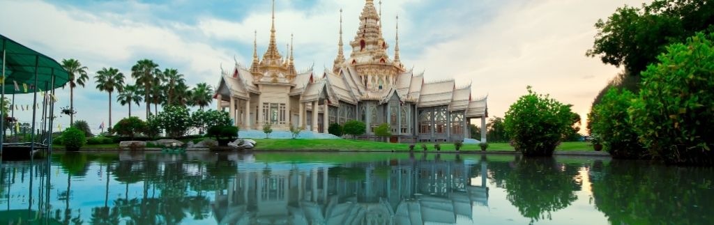 Tempio thailandese riflesso sull’acqua al tramonto, simbolo di serenità e del sogno di una pensione Thailandia tranquilla.