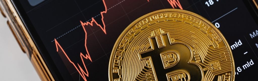 Nahaufnahme einer Bitcoin-Münze vor einem fallenden Kursdiagramm auf einem Smartphone – Symbolbild für Thailand Krypto und Marktvolatilität.