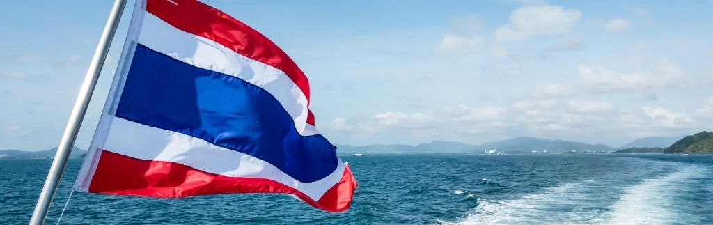 Bandiera della Thailandia che sventola sul mare azzurro, simbolo della libertà di vivere in Thailandia