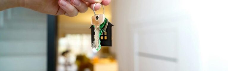 Personne tenant des clés attachées à un porte-clés en forme de maison, symbolisant l'immobilier en Thaïlande.