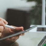 Professionista che firma su un tablet, con l'ambiente di lavoro moderno, mentre gestisce pratiche come il rinnovo del visto in Thailandia.