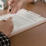 Two individuals signing a document with a house model and calculator, representing International Estate Planning.