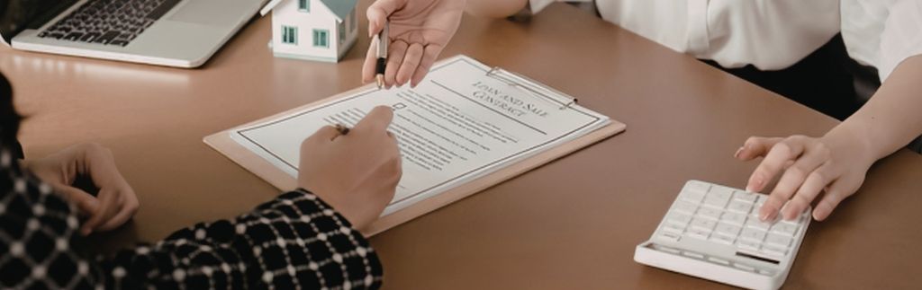 Two individuals signing a document with a house model and calculator, representing International Estate Planning.
