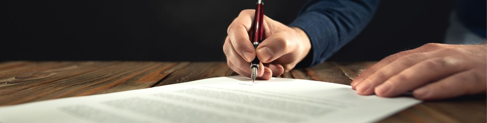 Man signing company documents with a fountain pen on a wooden desk