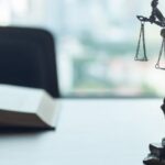 Statue de la justice placée sur un bureau devant un livre ouvert, représentant les services d’un avocat pour expatriés en Thaïlande.