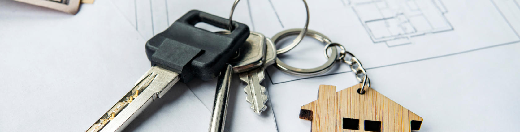 House keys with a wooden house keychain placed on real estate documents and cash, representing a property purchase or rental agreement.